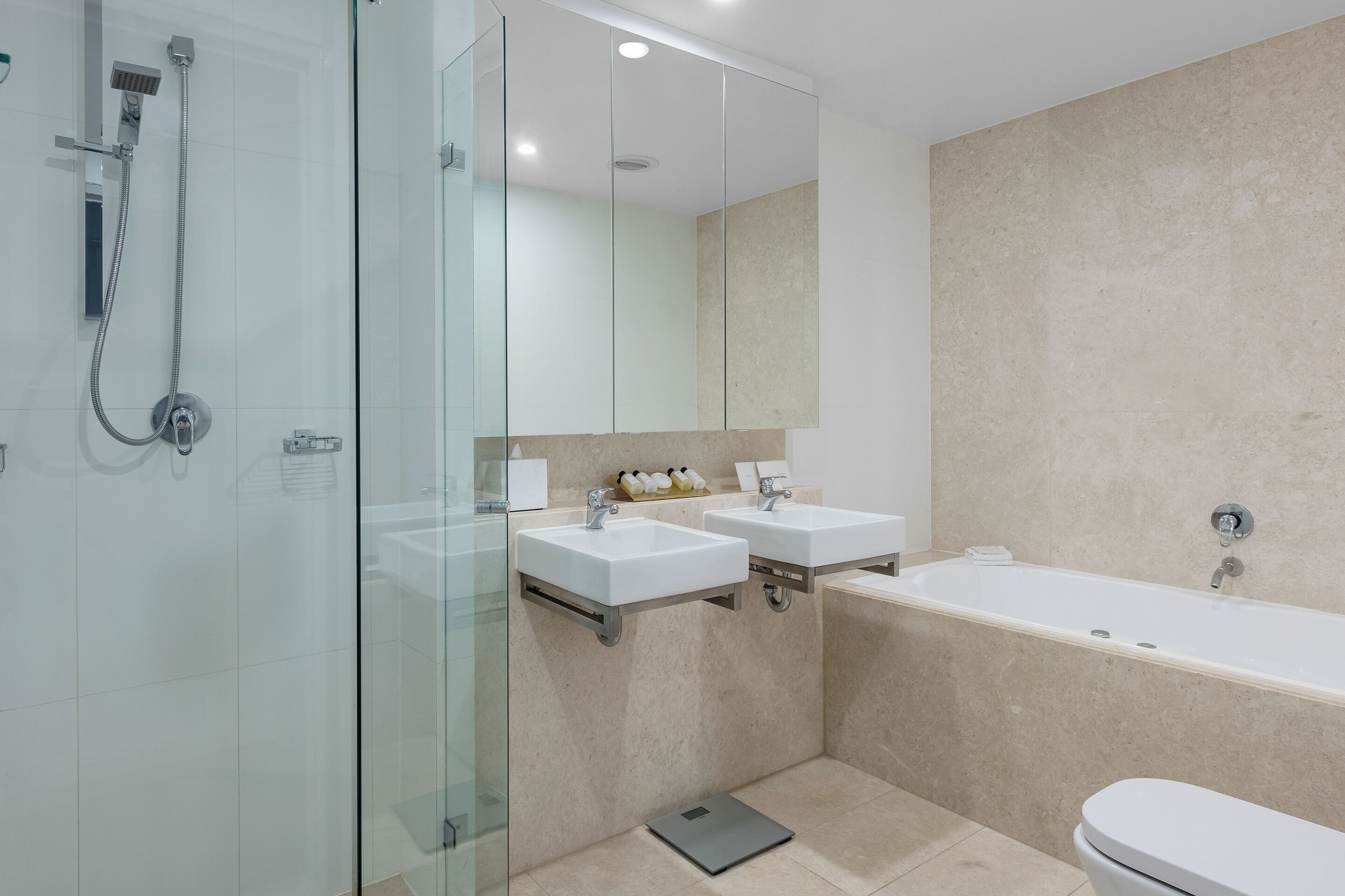 A modern bathroom with a glass shower enclosure, two sinks, a large bathtub, and a toilet.