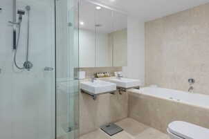 Un baño moderno con cabina de ducha de vidrio, dos lavamanos, una bañera grande y un inodoro.