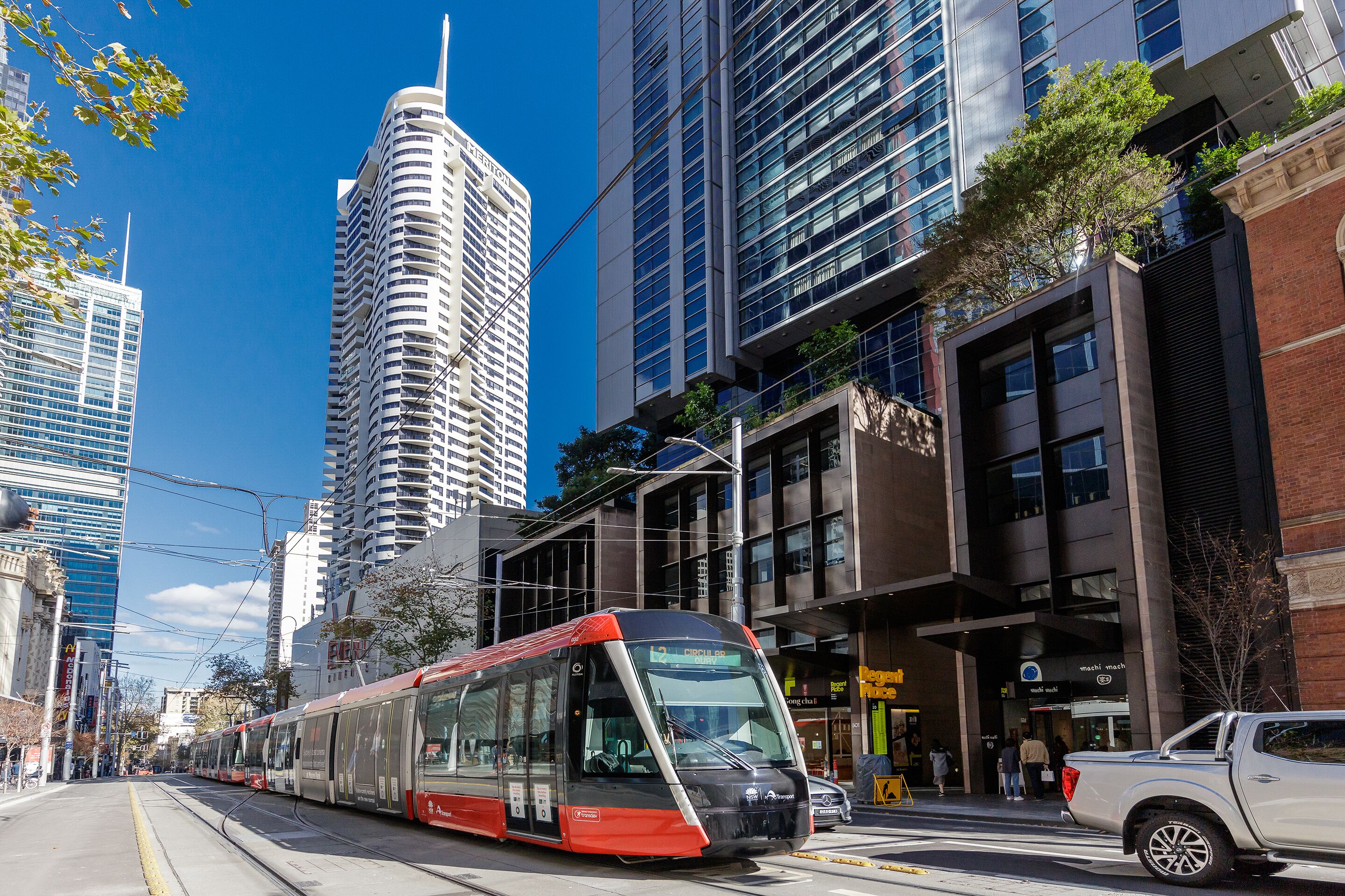 Una calle urbana moderna con un tranvía rojo y negro, edificios altos y una combinación de edificios comerciales y residenciales.