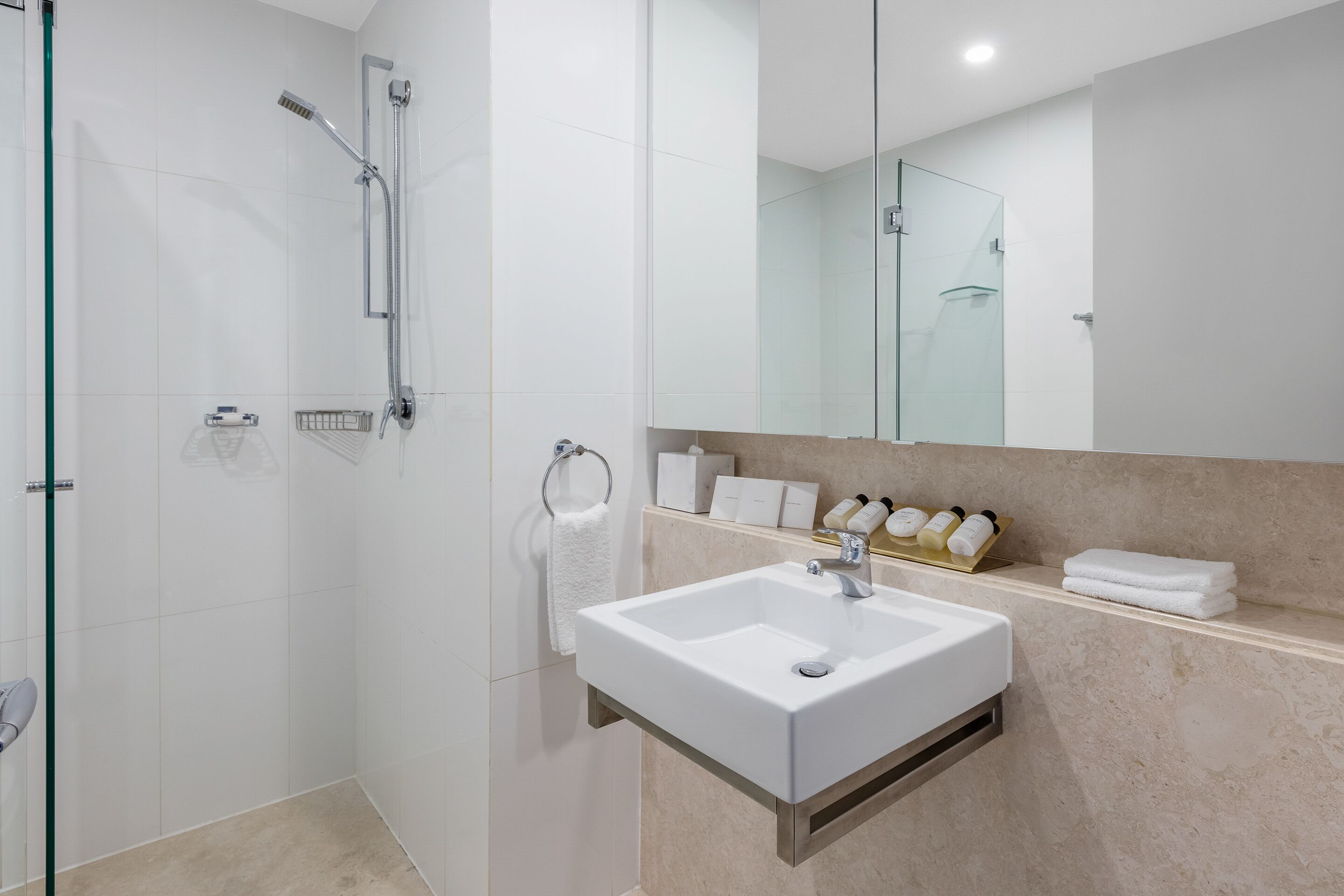 A modern bathroom with a glass shower enclosure, a white sink, and a marble countertop.