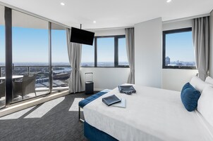 Ein modernes Hotelzimmer mit einem großen Bett, einem Schreibtisch, einem Laptop und Blick auf die Stadt.
