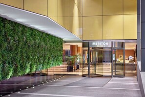 Entrada de un hotel con puerta de cristal, un jardín vertical verde y un cartel que indica Meriton Suites.