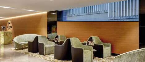A modern hotel lobby with seating areas, a reception desk, and a decorative wall.