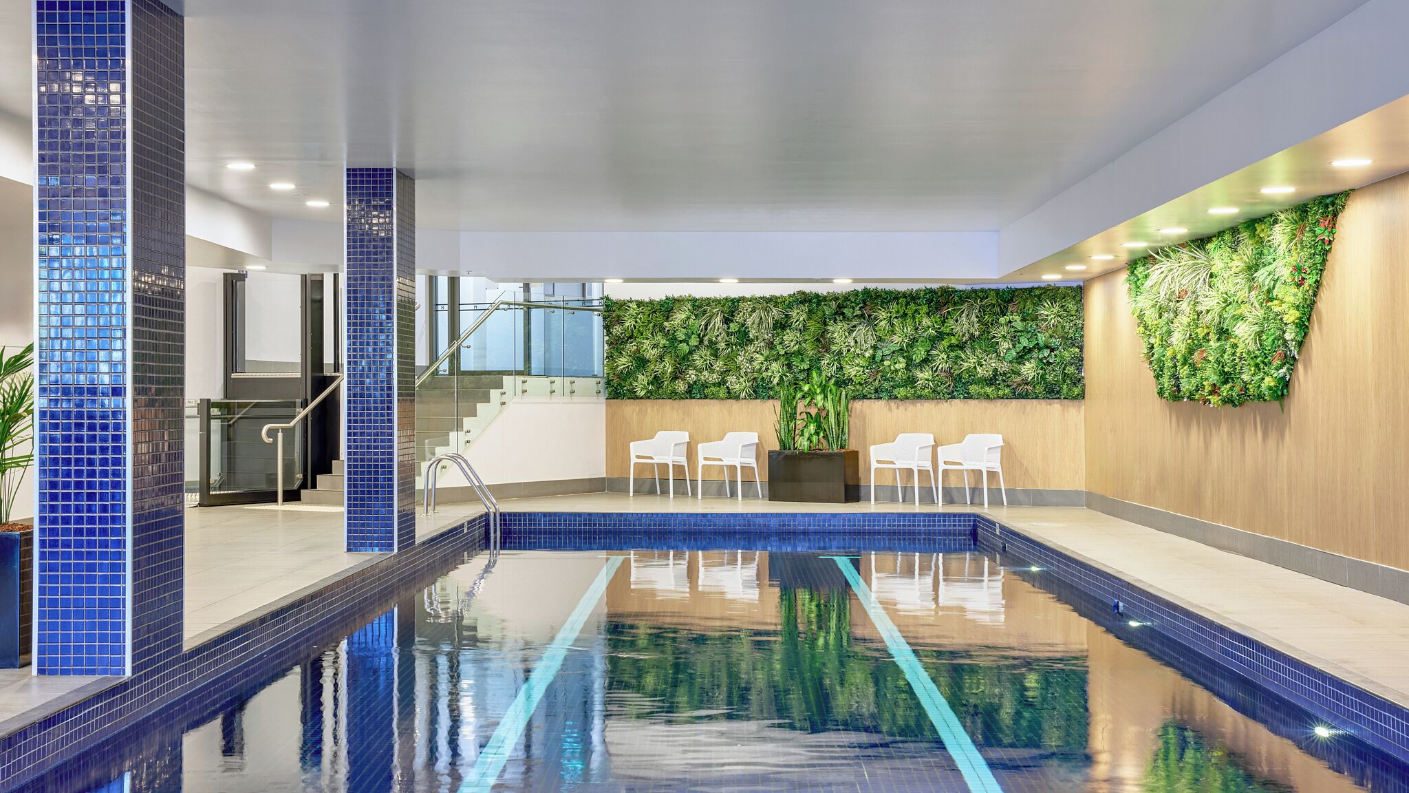 An indoor swimming pool with a tiled floor, a staircase, and a wall with a vertical garden.