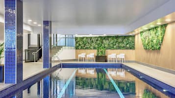 An indoor swimming pool with a tiled floor, a staircase, and a wall with a vertical garden.