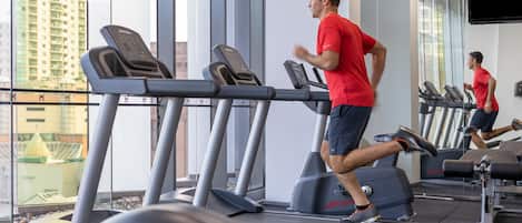 A gym with treadmills and weights, large windows, and a city view.