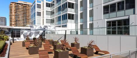 A rooftop terrace with wooden seating, planters with plants, and a geometric wall design.
