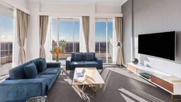 Ein modernes Wohnzimmer mit Sofa, Couchtisch und Fernseher, großen Fenstern mit Vorhängen und Blick auf die Stadt.