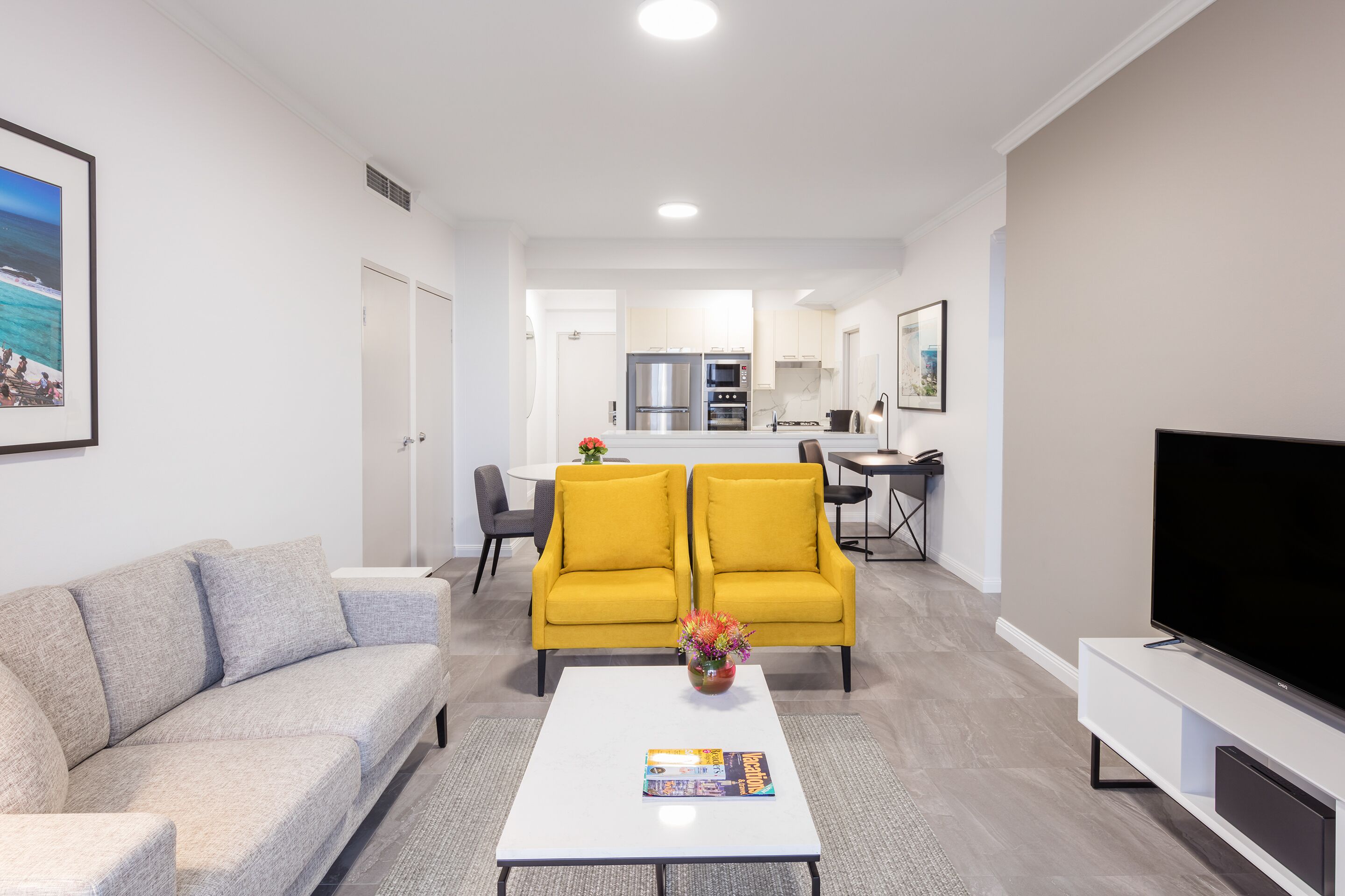 A modern living room with a sofa, a coffee table, a TV, and a dining area in the background.