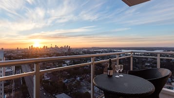 Un balcón con mesa y sillas, con vista a un paisaje urbano al atardecer.