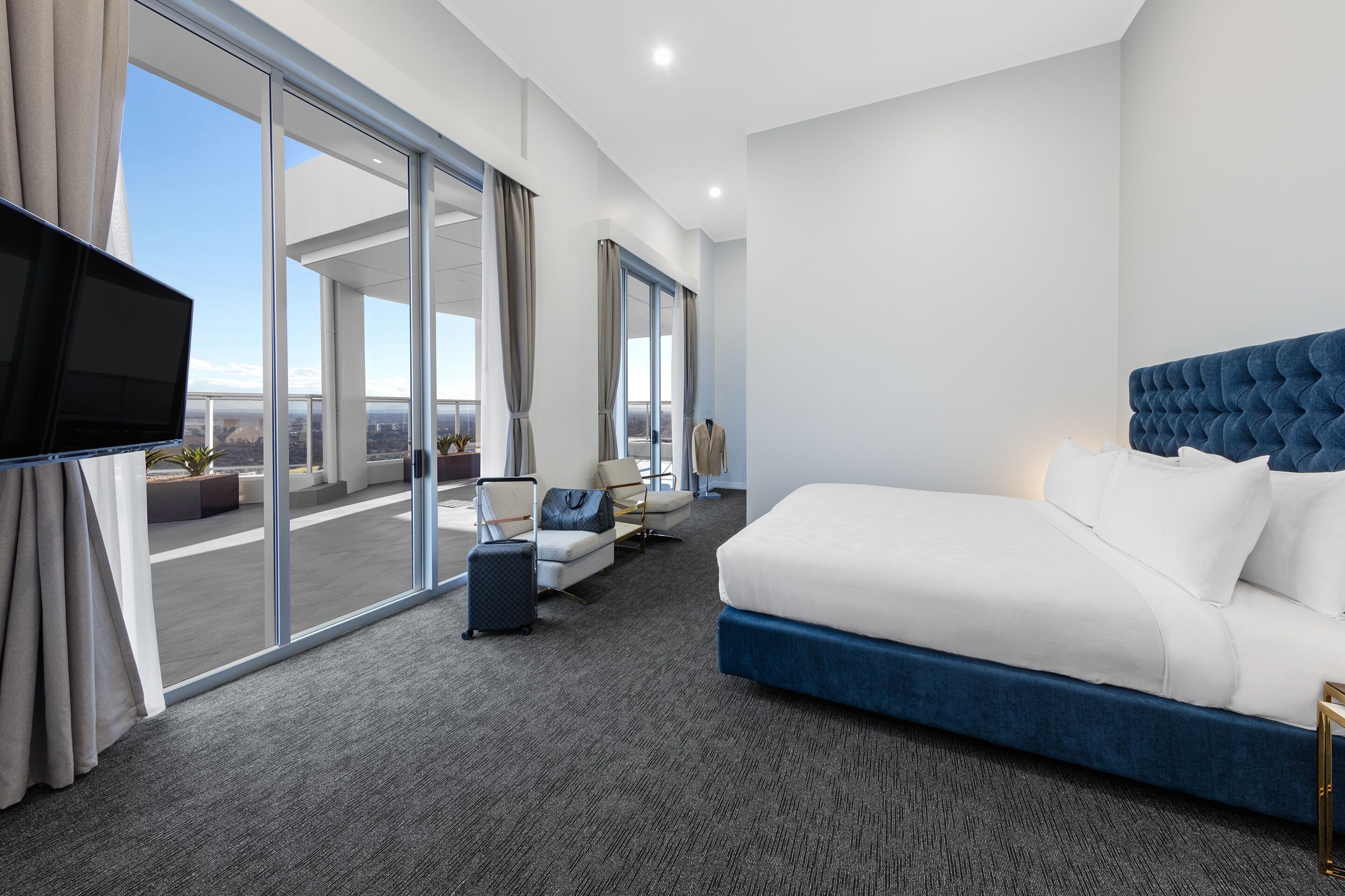 A modern hotel room with a large bed, a flat-screen TV, a sofa, and a view of the city.