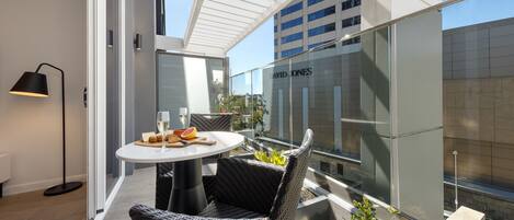 A modern outdoor dining area with wicker chairs and a round table, overlooking a cityscape and a building with 'DAVID JONES' signage.