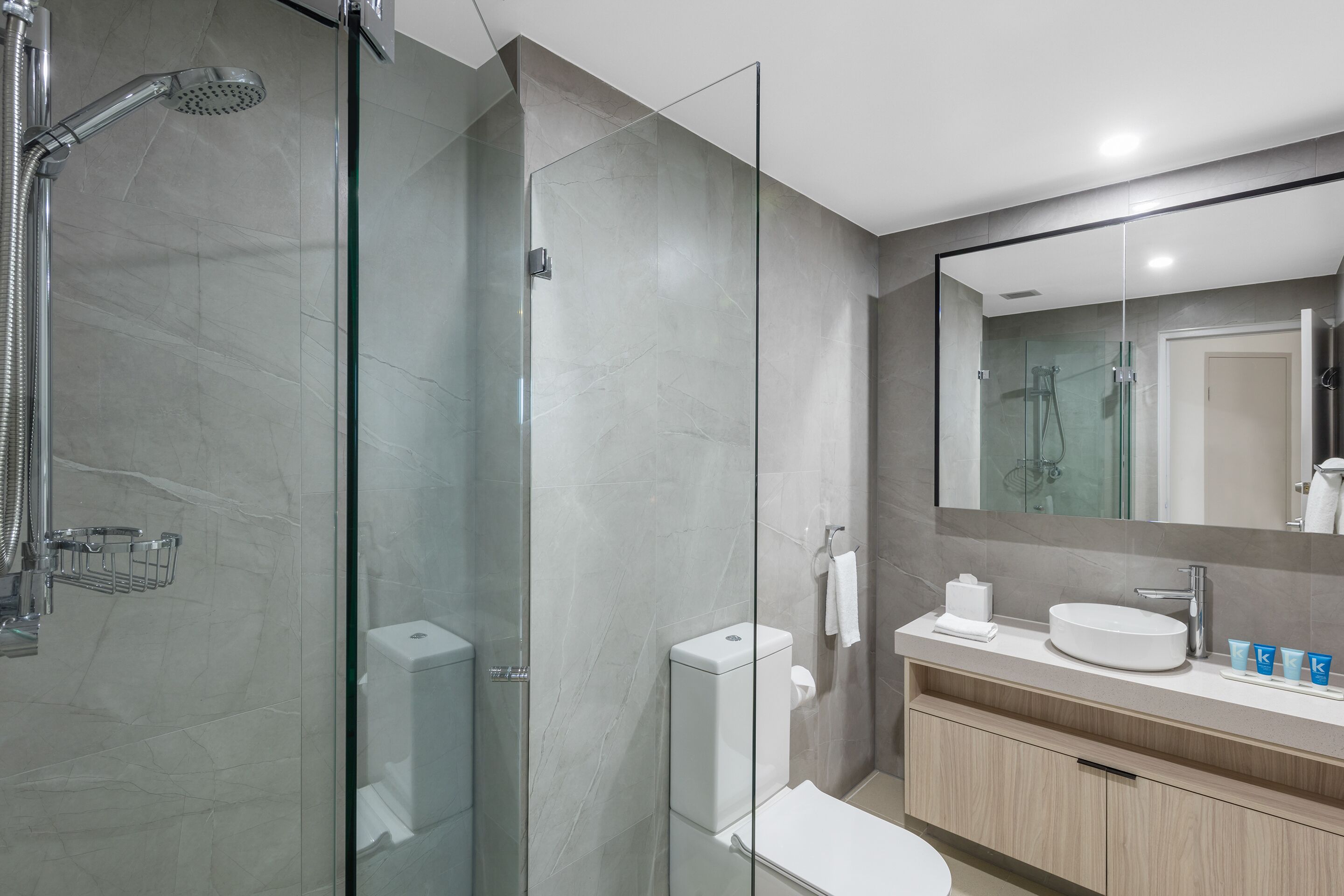 Une salle de bain moderne avec une douche à parois de verre, des toilettes, un lavabo avec un miroir et un porte-serviettes.