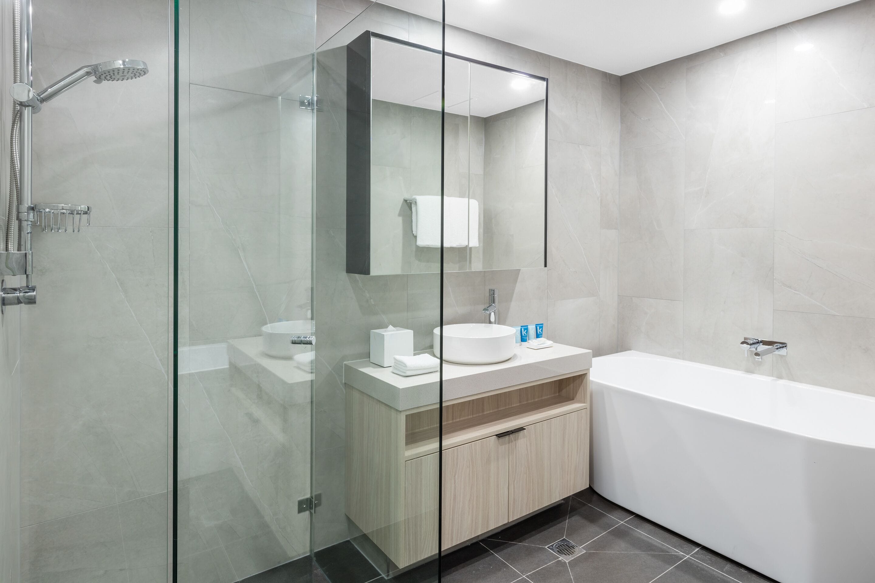 Ein modernes Badezimmer mit einer Glaskabine zur Dusche, einer freistehenden Badewanne und einem Waschtisch mit Spiegel.