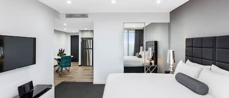 A modern hotel room with a large bed, a flat-screen TV, a desk, and a dining area.
