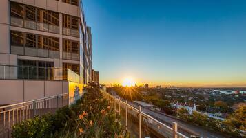 A modern building with multiple floors and large windows, overlooking a busy road and a cityscape during sunset.
