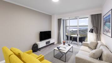 A modern living room with a sofa, yellow armchairs, a coffee table, a flat-screen TV, and a balcony with a city view.