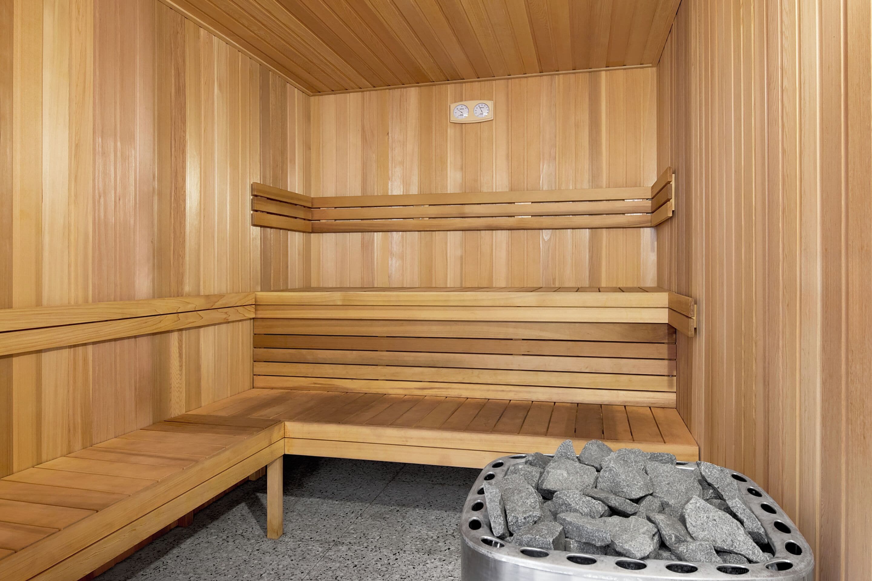 A sauna with wooden benches and a metal container filled with stones.
