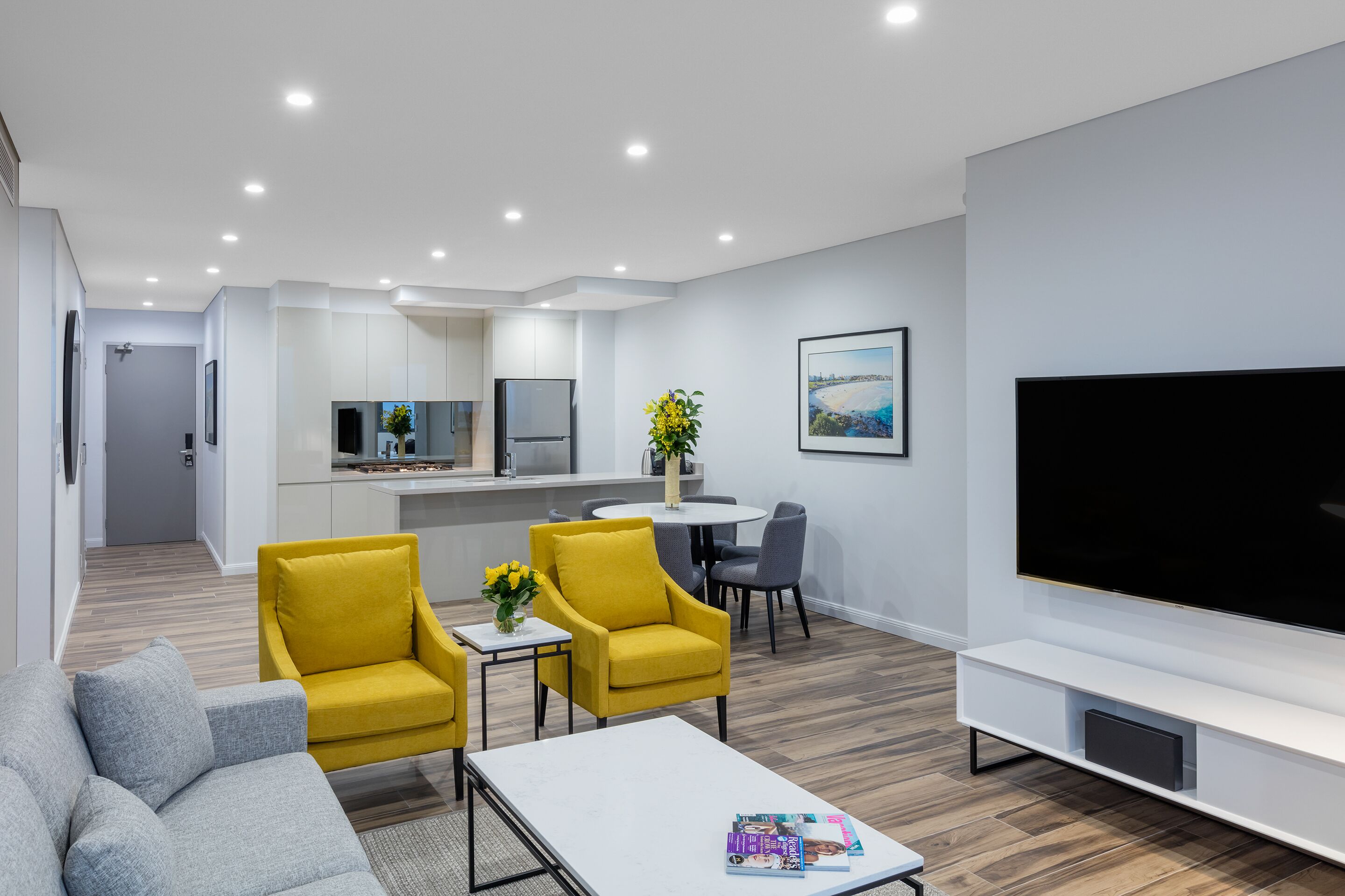 Una sala moderna con un sofá, sillones amarillos, una mesa de centro y un televisor.