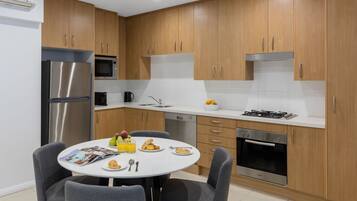 A modern kitchen with wooden cabinets, stainless steel appliances, and a dining area with a round table and chairs.