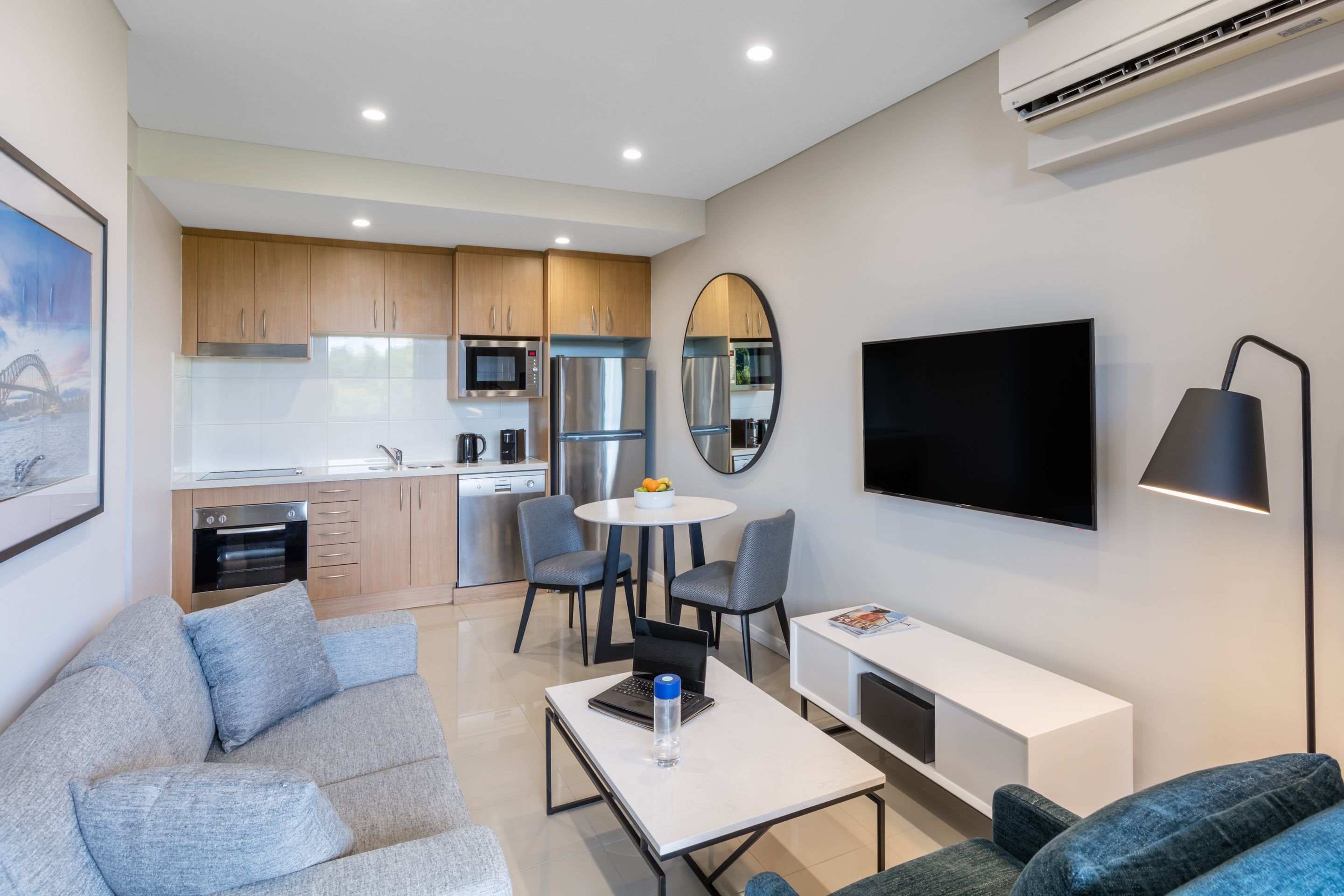 Una sala de estar moderna con un sofá gris, una mesa de centro blanca y un televisor de pantalla plana montado en la pared.