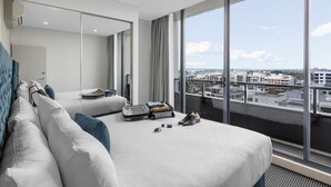 Ein modernes Hotelzimmer mit einem großen Bett, einem Koffer und Blick auf die Stadt durch große Fenster.