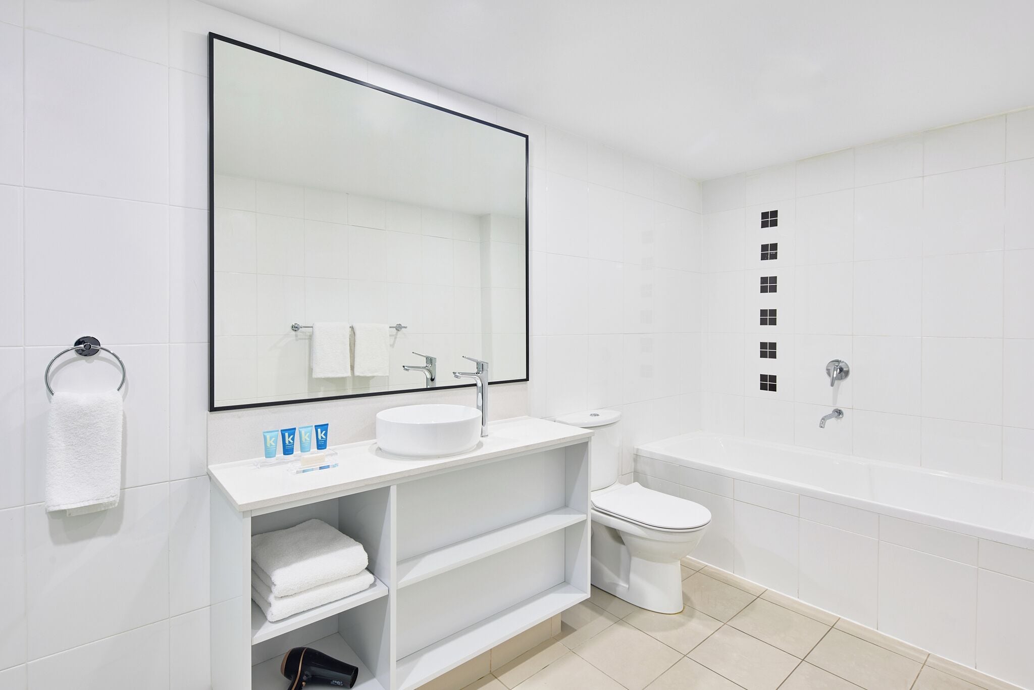 Un baño moderno con un espejo grande, lavamanos blanco, inodoro y bañera.