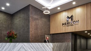 Ein moderner Hotel-Empfangsbereich mit einer Marmor-Rezeption, einer Holzwand mit dem Hotelnamen und einer zeitgemäßen Leuchte.