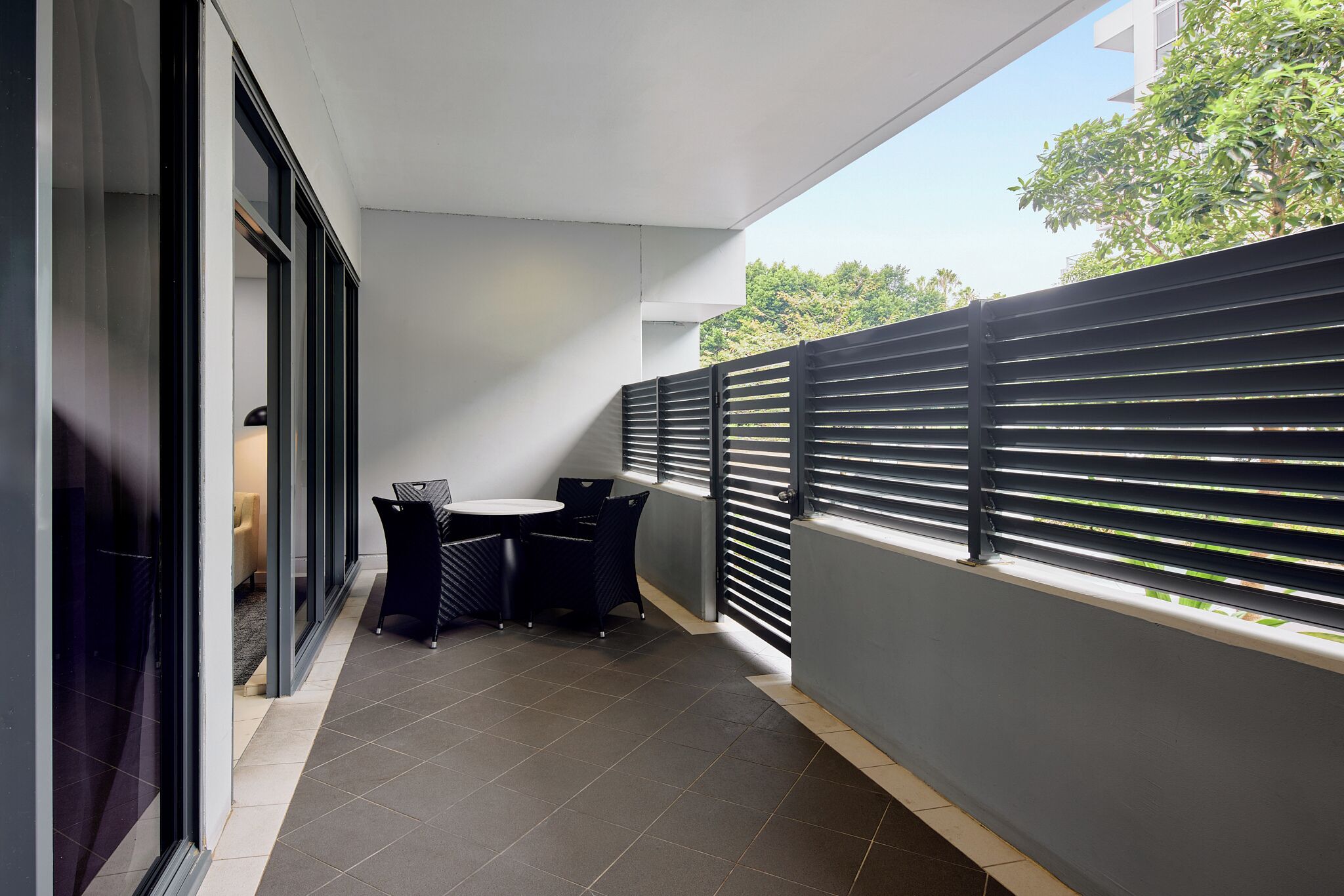 A balcony with a table and chairs, a view of greenery, and a modern building facade.