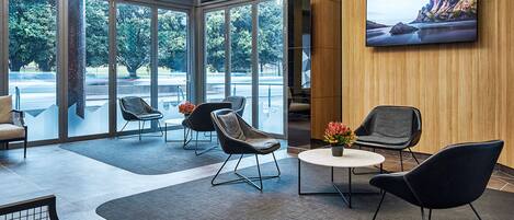 A spacious lobby with modern seating, large windows, and a flat-screen TV on the wall.