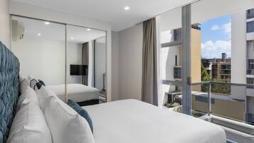 A modern hotel room with a large bed, a TV, and a balcony with a city view.
