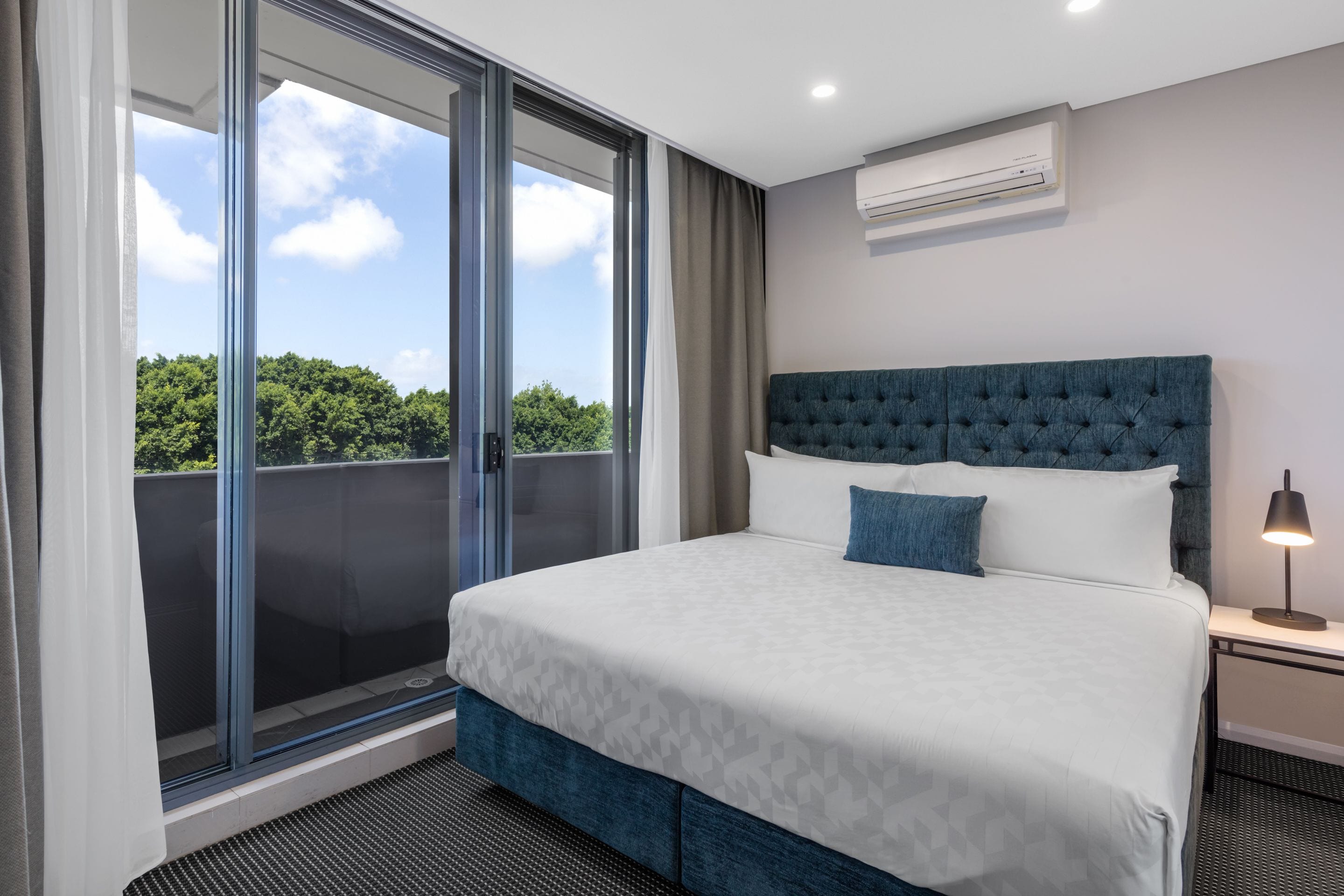 Een hotelkamer met een groot bed, een nachtkastje, een airconditioning en uitzicht op groen buiten het raam.