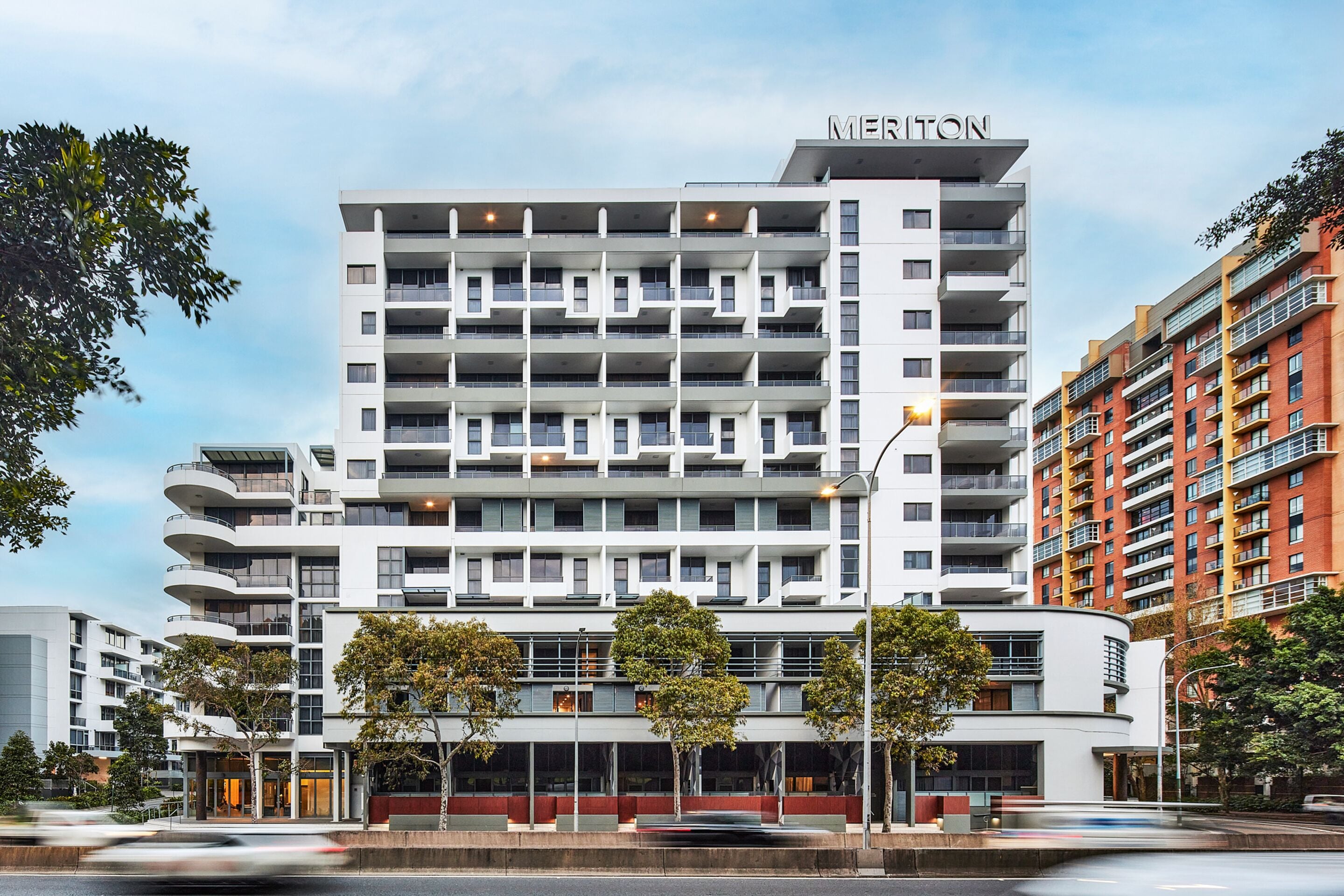 Un hôtel à plusieurs étages au design moderne, doté de balcons et d’une enseigne « MERTON » bien visible.