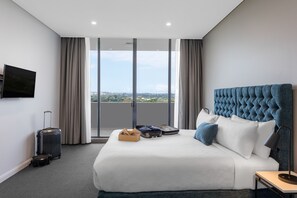 Une chambre d’hôtel avec un grand lit, un téléviseur à écran plat, une valise et une vue sur la ville.