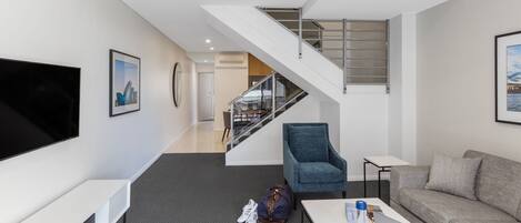 A modern hotel room with a flat-screen TV, a sofa, a desk with a laptop, a chair, and a staircase leading to an upper level.