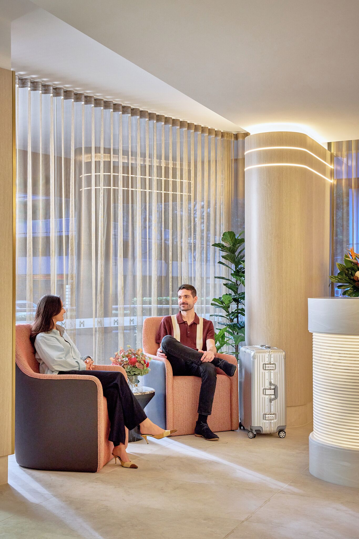 Un hall d’hôtel moderne avec un espace salon, une grande fenêtre avec des rideaux et un comptoir d’accueil.