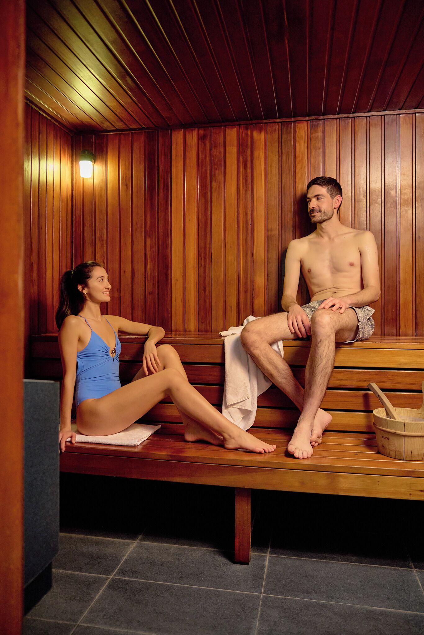 A sauna with wooden benches, a towel, and a bucket.
