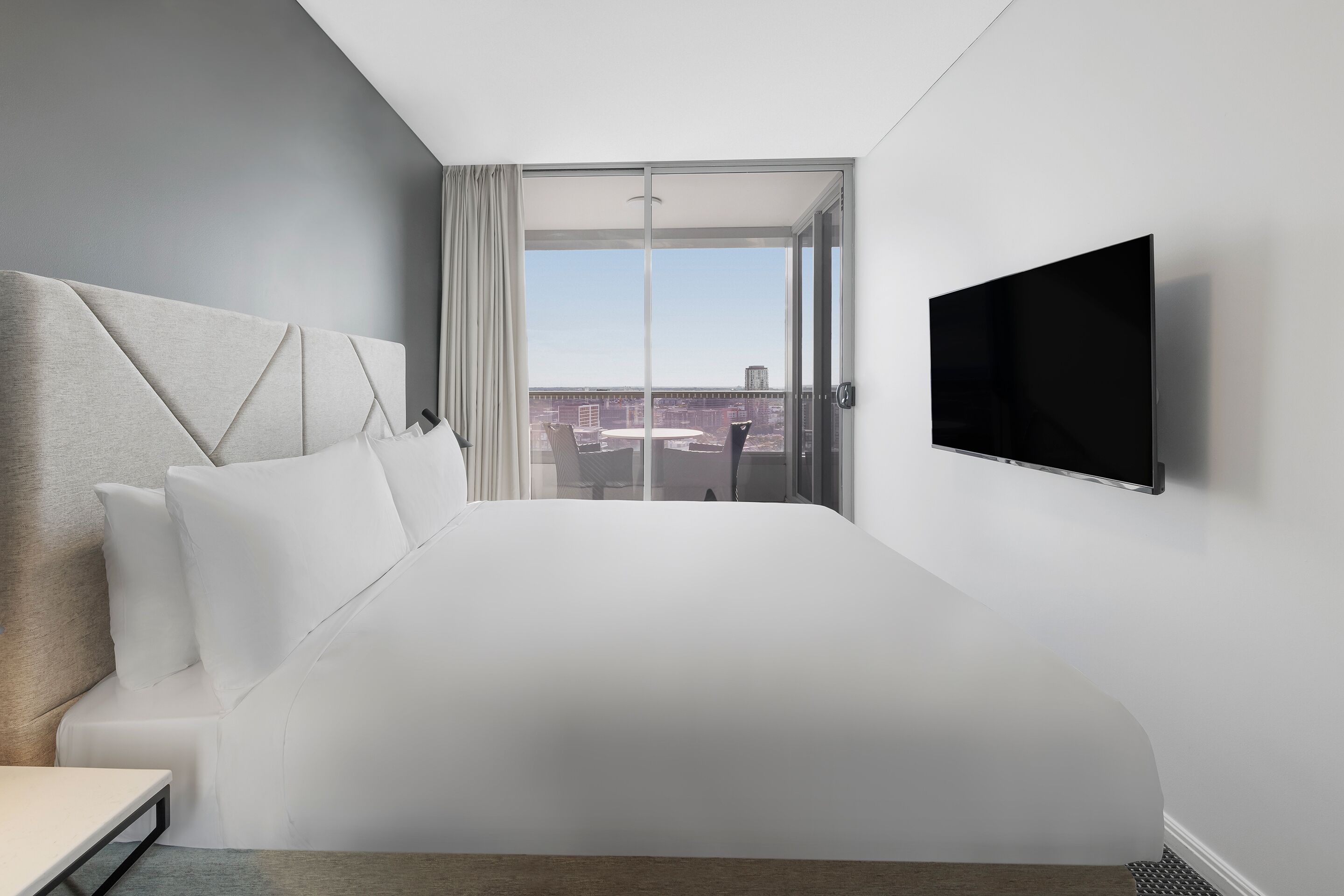 A hotel room with a large bed, a flat-screen TV, and a sliding glass door to the outside.