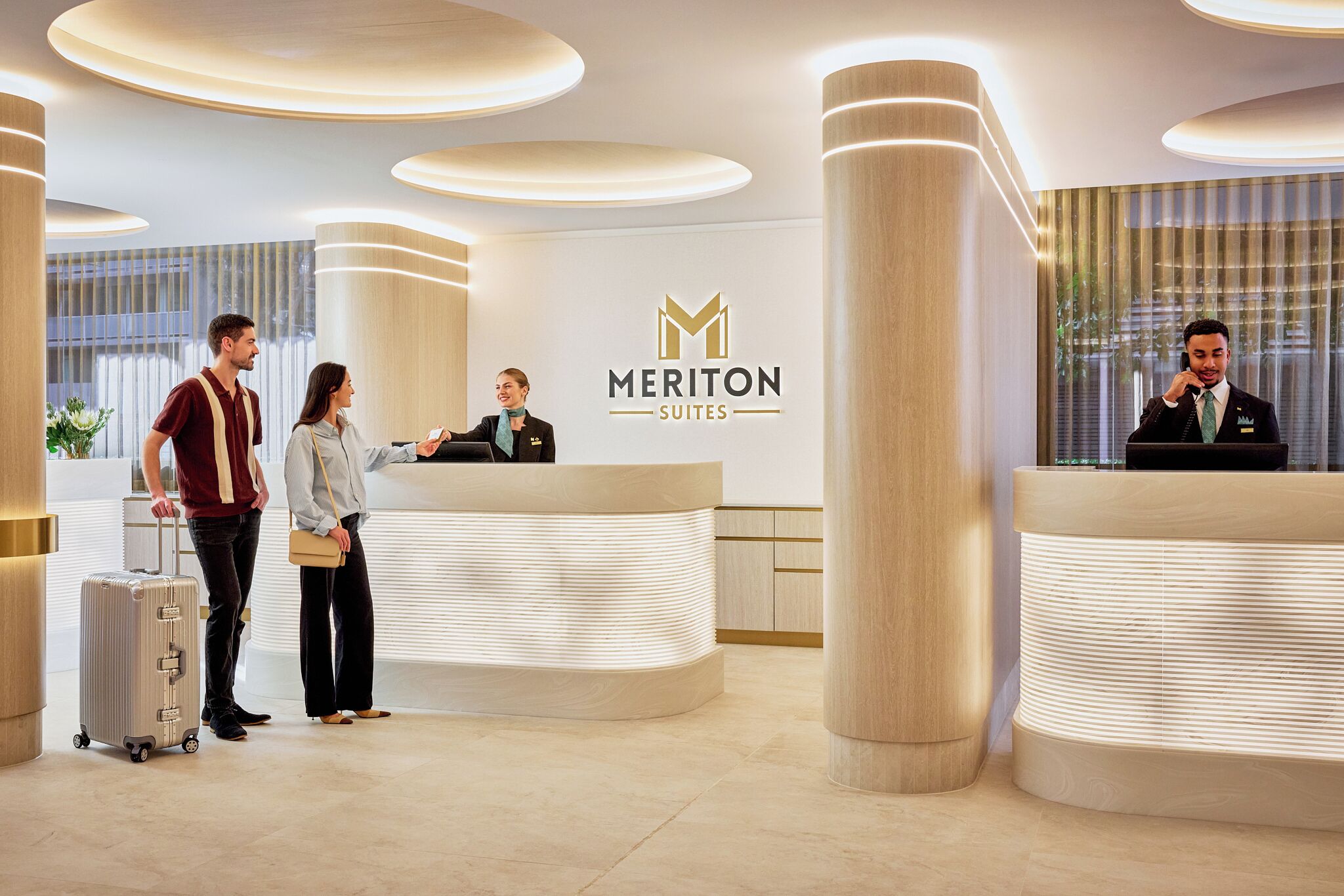 A hotel reception area with a modern design, a reception desk, and a logo for Meriton Suites.