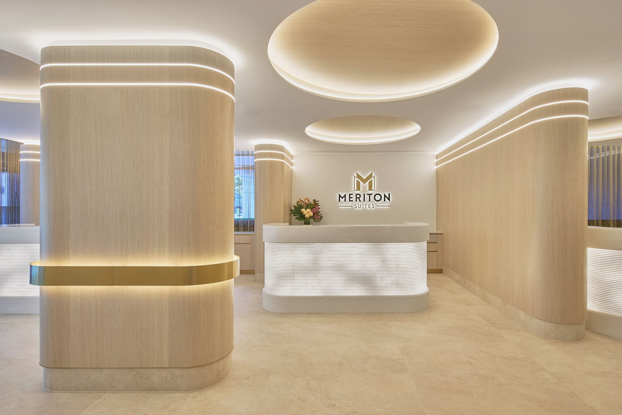 Ein Empfangsbereich im modernen Stil mit einer Rezeption, großen zylindrischen Säulen und dem Logo von Meriton Suites.