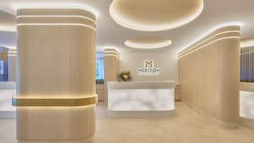 Ein Empfangsbereich im modernen Stil mit einer Rezeption, großen zylindrischen Säulen und dem Logo von Meriton Suites.
