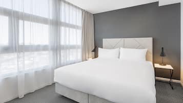 Una cama bien hecha con sábanas blancas, un cabecero gris y dos lámparas de noche.