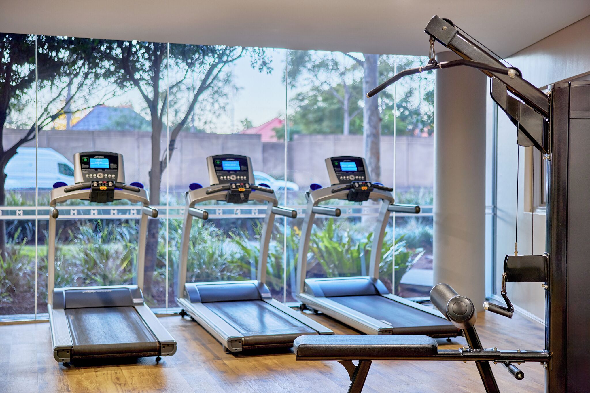 Una palestra con tapis roulant, panchina per pesi e una finestra che si affaccia su alberi e una recinzione.