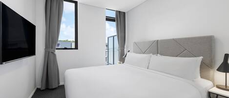 Een moderne hotelkamer met een groot bed, een flatscreen televisie, een nachtkastje met lamp en een raam met gordijnen.