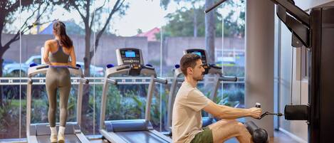Un gimnasio con cintas de correr, una máquina de remo y una persona usando la máquina.