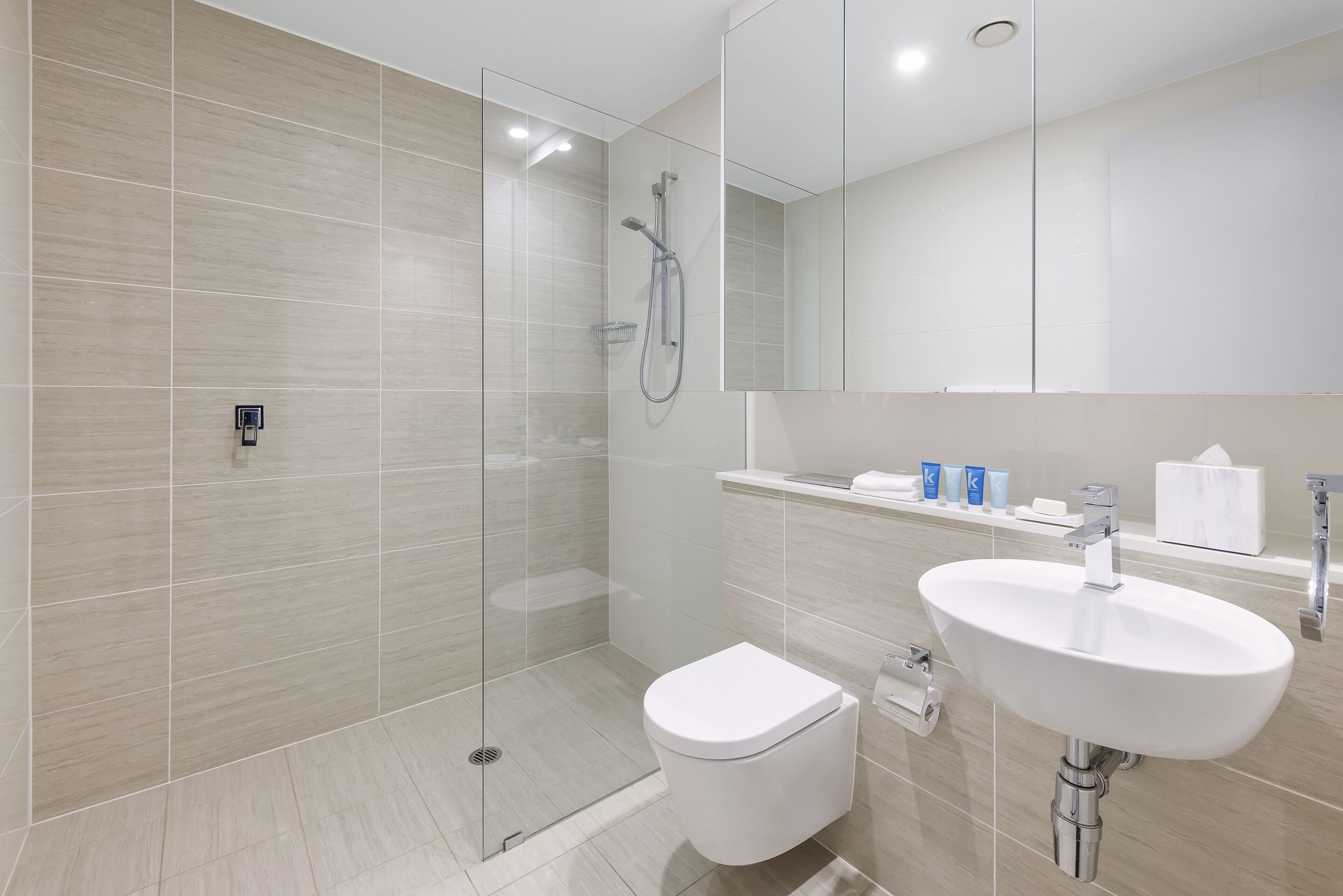 Une salle de bain moderne avec une douche à parois de verre, des toilettes blanches et un lavabo avec un miroir au-dessus.