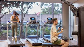 A gym with treadmills, a bench press, and a view of trees and a fence.