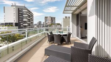 Un balcon doté d’une balustrade en verre, de mobilier d’extérieur et offrant une vue sur les bâtiments environnants.