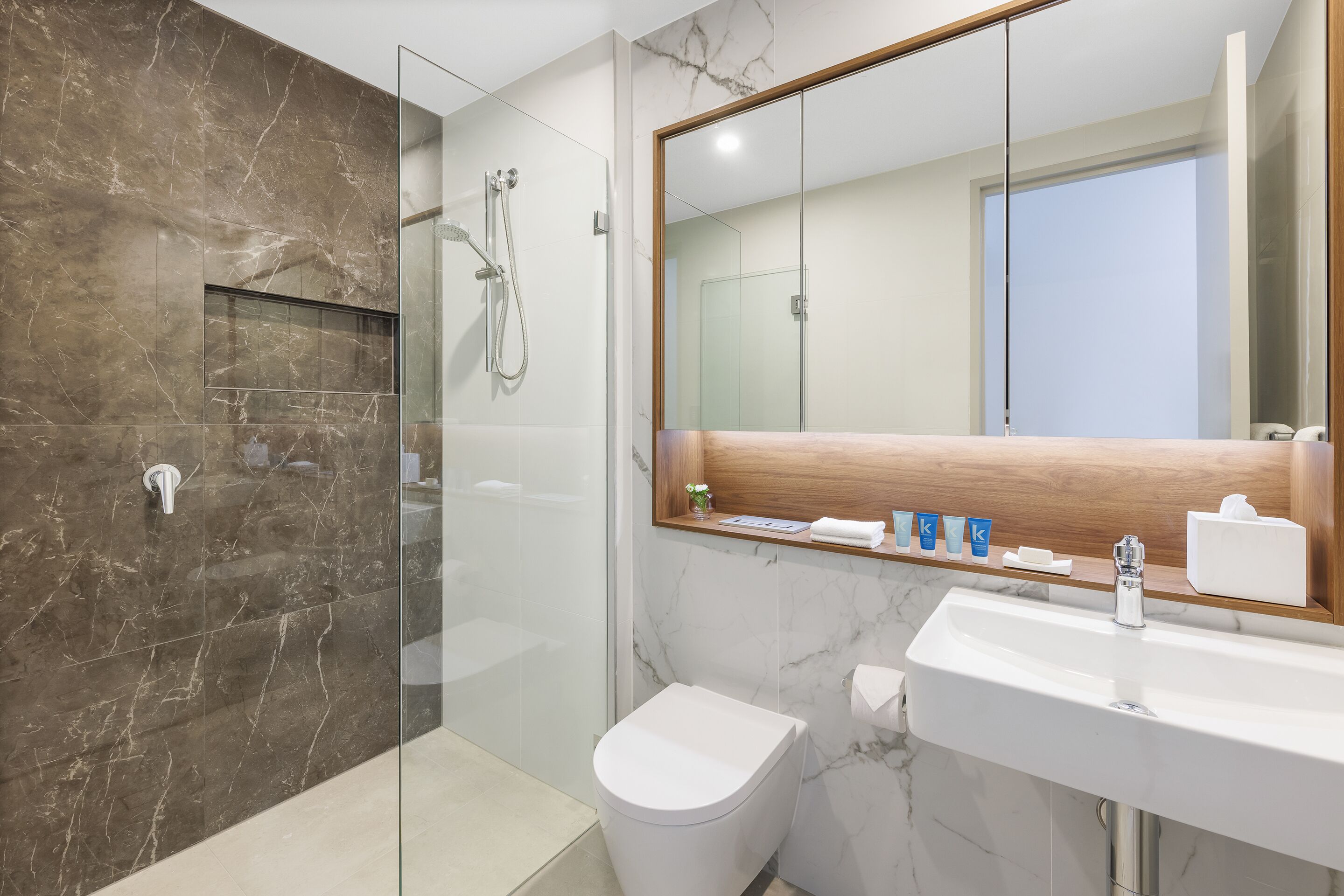 A modern bathroom with a glass-enclosed shower, a white toilet, and a marble sink.