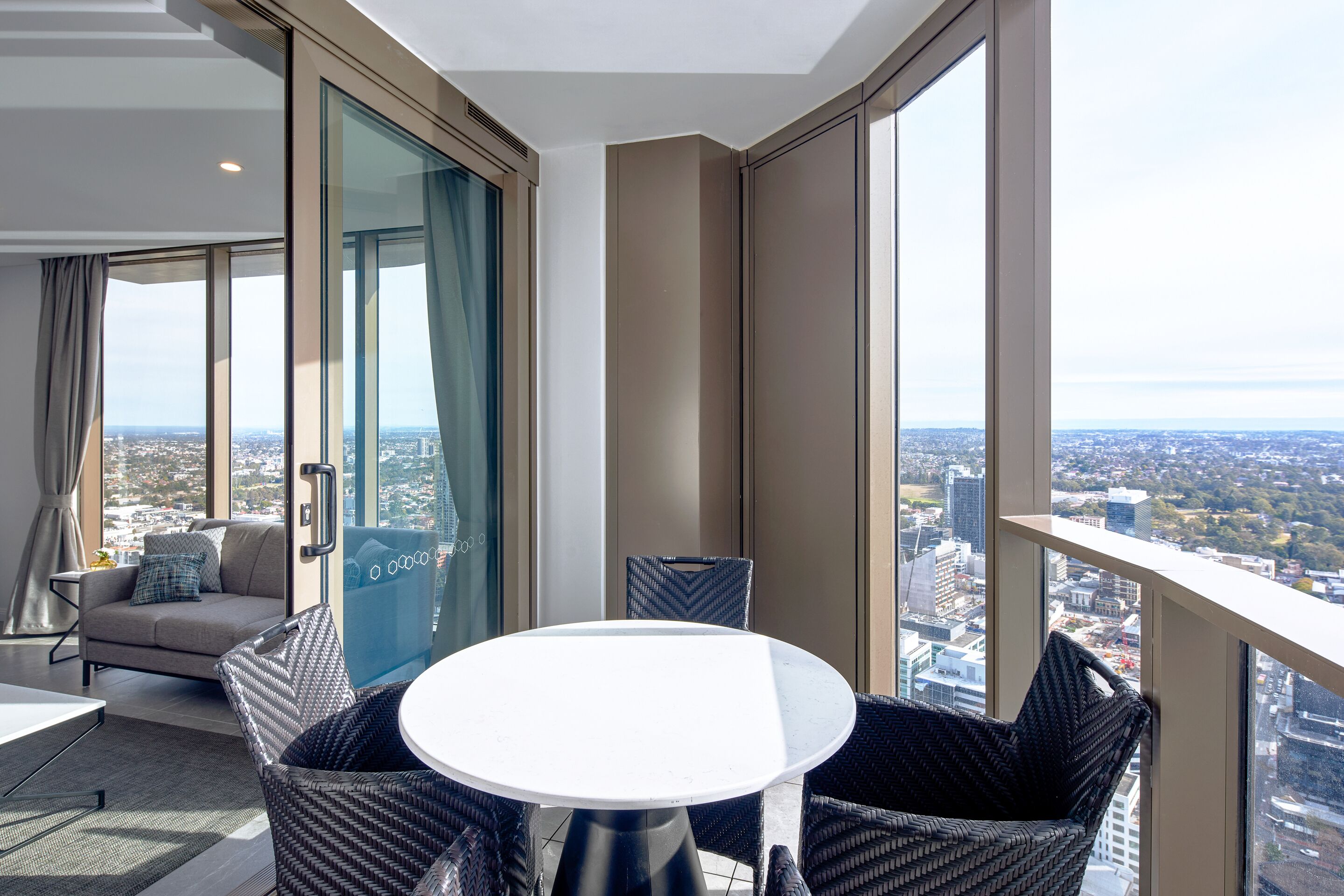 A balcony with a round table and wicker chairs, overlooking a cityscape.